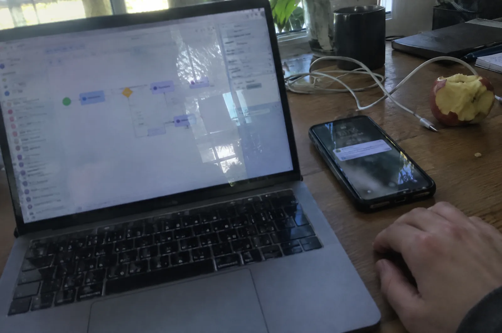 Laptop op een bureau met een schema van verbonden blokken op het scherm, ernaast een telefoon met een goedkeuringsmelding