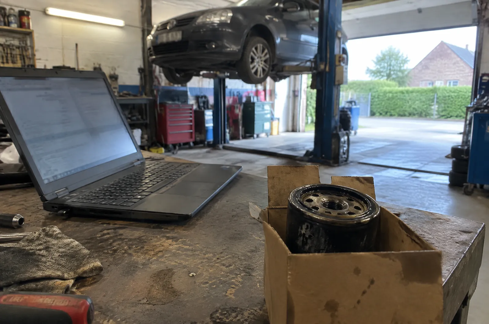 Laptop op een werkbank in een garage, naast een nieuw oliefilter in een doos
