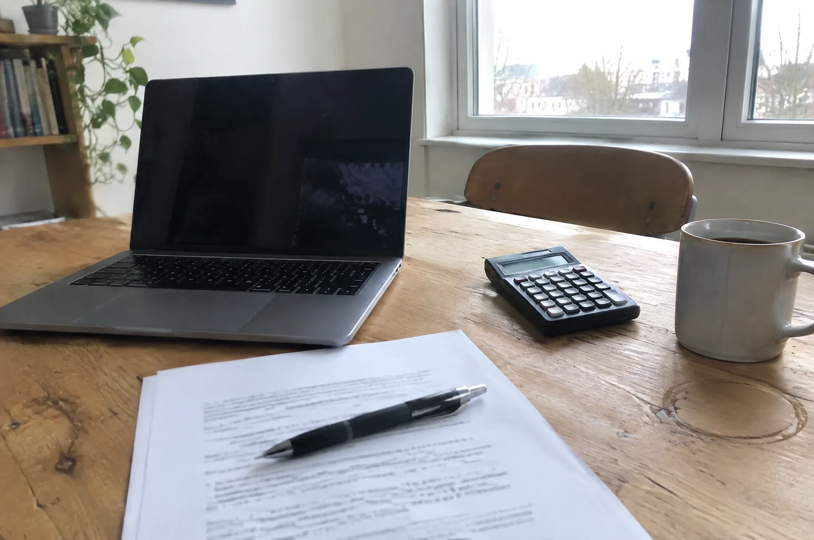 Laptop, rekenmachine en een uitgeprinte offerte op een houten tafel in een kantoor